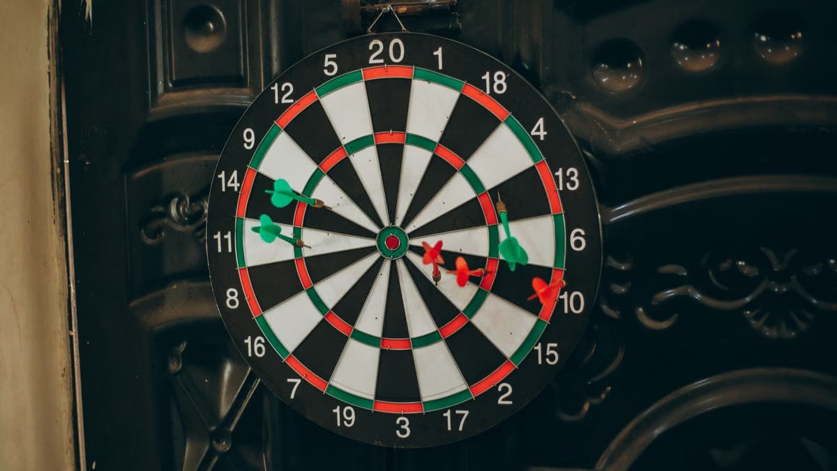 Close-up of a dartboard with red and green darts hitting various spots, indoors setting.